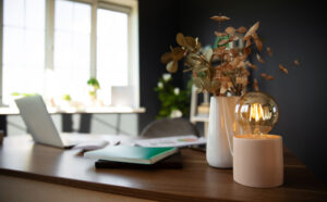 Bureau lumineux avec ordinateur portable, carnet, documents et lampe décorative, évoquant un espace de travail soigné pour la rédaction web, la correction et la relecture.