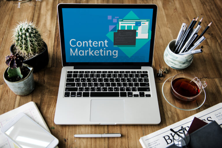 Ordinateur portable affichant le terme Content Marketing sur un bureau avec carnet, crayons et tasse de thé, évoquant la rédaction web, la stratégie de contenu et la communication digitale.