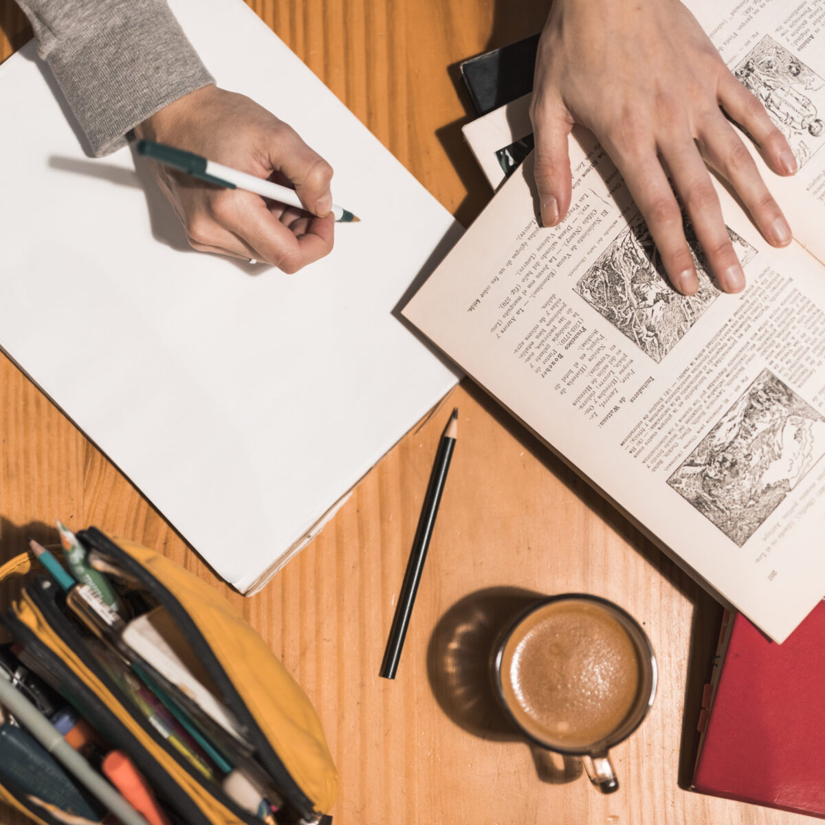 Personne prenant des notes à côté d’un livre ouvert et d’une tasse de café, évoquant le travail de relecture, de correction et de rédaction.