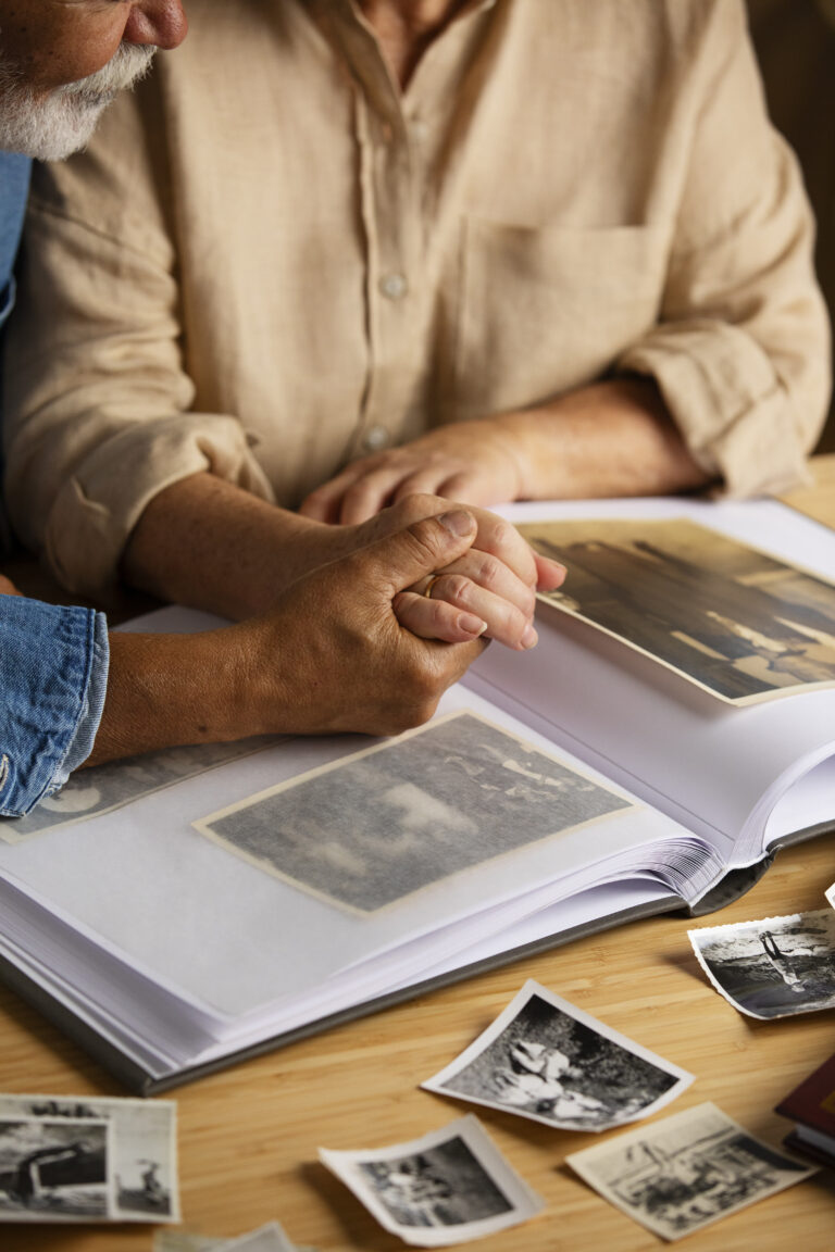 Deux personnes feuillettent un album de famille entouré de photographies anciennes.