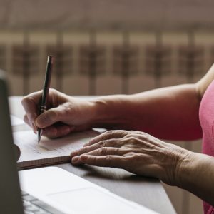 Femme prenant des notes dans un carnet à côté d’un ordinateur portable.